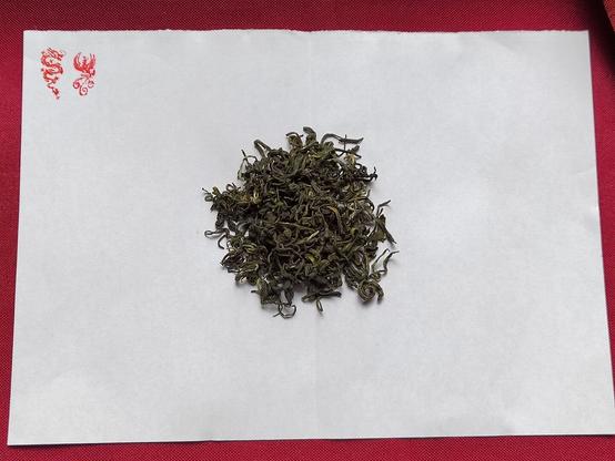 This is a closeup of the tea leaves on the slip of paper, vermillion stamps of a dragon and a "phoenix" decorating the top left corner.  As with any Cloud and Mist tea the leaves are tightly rolled and very sinuous.  There's a good degree of the silver tippy leaves in the mix and no hint of chop or stem.  The production quality of this tea is top notch.