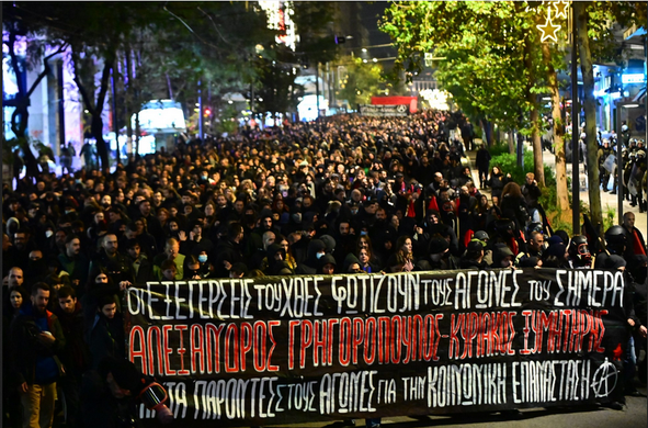 Bild einer riesigen Menschenmenge welche vorn einen Banner mit griechischer Aufschrift trägt