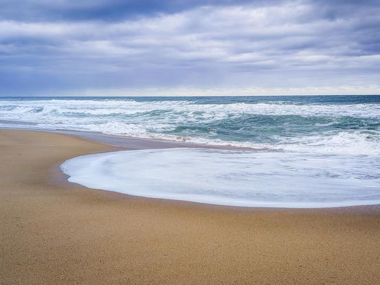 The rounded surf of a receding wave contrasts with an azure blue sky at a dreamy Pennington Beach in KwaZulu-Natal, South Africa 🇿🇦