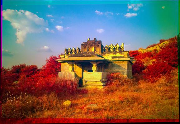 An infrared trichrome photo of a stone temple. The ir makes the surrounding foliage bright red.