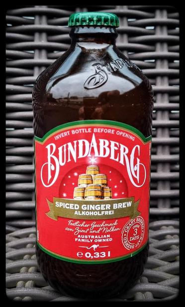 Eine Flasche Bundaberg spiced ginger beer vir dunklem Hi tergrund, das Etikett ist rot, in der Mitte sind Jolzfässer mit einem western darüber und stilisierte Schneeflocken drumrum zu sehen