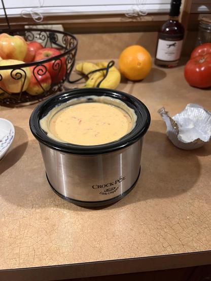 Photo of a mini crockpot full to the brim with an orangish cheese mixture. Bits of salsa can be seen mixed in.