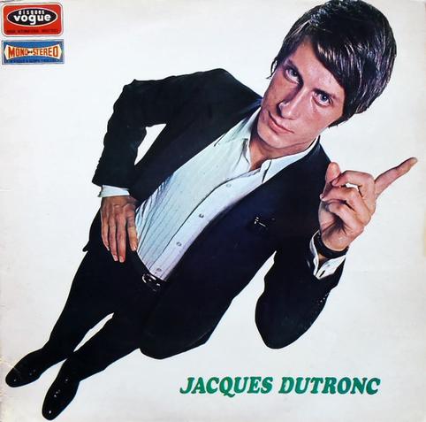 The album cover is a photo of the artist, a white man with brown hair wearing a black or dark blue slim fitting suit with a white striped button-up shirt underneath. His right hand is on his hip, his left pointing up with his index finger, and he is looking up at the camera. The perspective is a bit odd, as the camera is above his head and pointed down, so his head looks larger than it should. The photo is on the diagonal so his head is in the top right corner, his feet in the bottom left. The artist's name is in green font in the bottom right corner (there is no album title).