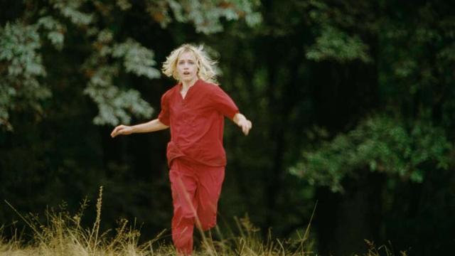 A woman with a terrified expression on her face running towards the camera from a forest behind her.