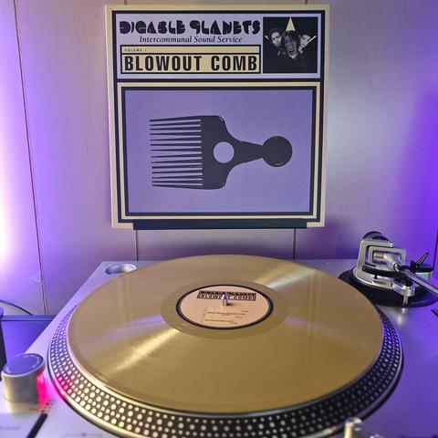 A gold vinyl record sits on a turntable. Behind the turntable, a vinyl album outer sleeve is displayed. The front cover shows afro pick, and a small picture of the 3 members. Text on the cover says:

Digable Planets
Intercommunal Sound Service
Volume 1
Blowout Comb
