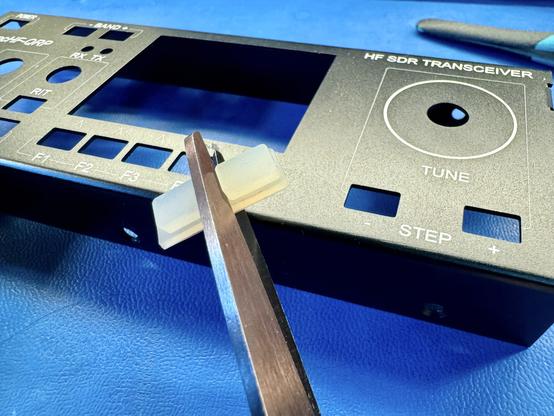 The front of the mcHF enclosure in the background. In the foreground there are scissors holding two silicone buttons in a strip.