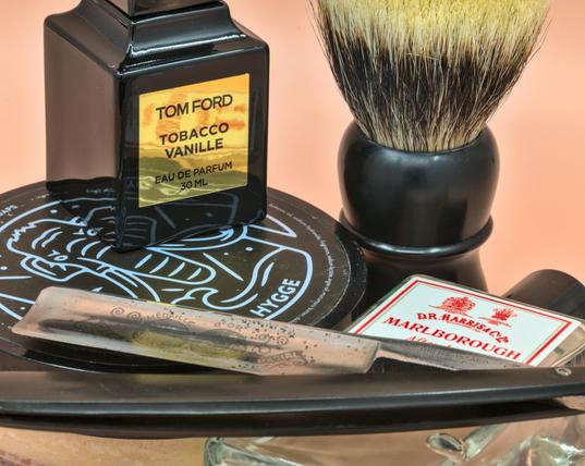 A big TI 14 blade lying over a bottle of DRH Marlborough splash and a tub of HoM Hygge with a bottle of TF Tobacco Vanille frag and a Dogclaration Mystery B16 brush