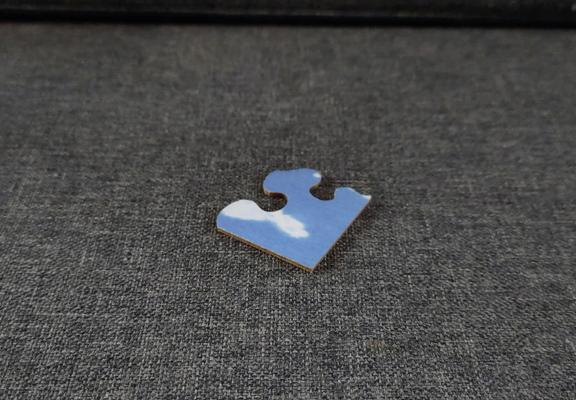 A piece of a jig saw puzzled blue like the sky with part if a white cloud on it.
