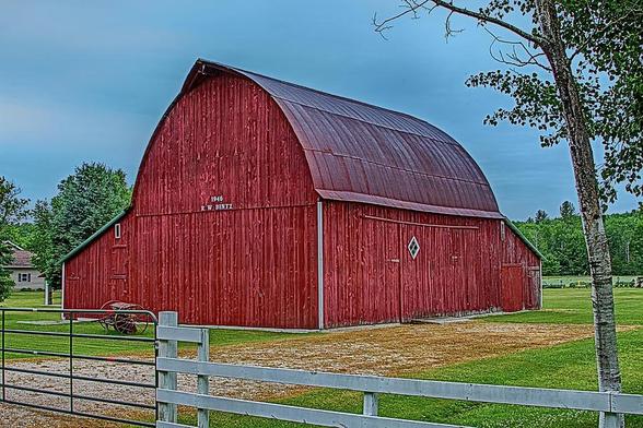 Big Red Barn at Cross Village

This is a big red barn near the edge of a road in the small enclave known as Cross Village in Northern Michigan.
The foreground consist of a wood fence and a steel gate that leads to the driveway into the farm. 
The right side of the image is framed with a tall birch tree. 
The barns walls are roughly 20 feet tall on the near side. On the far side of the barn the roof changes pitch at roughly 45 degrees. The roof of the barn is tall and curved to meet at the center of the building. 
The walls and the roof both are painted red and is weathered. 
In the background is a large pasture bordered by trees.