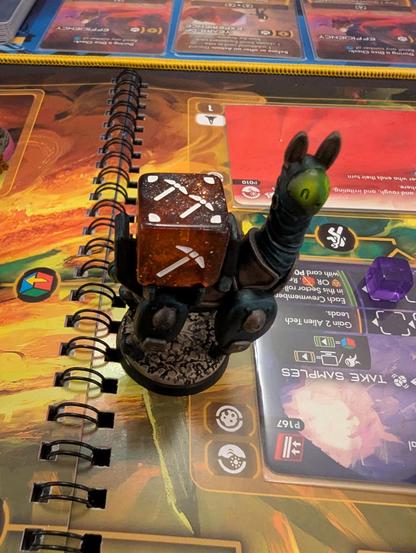 Game board with close-up of a mini. It's an alpaca carrying a red die on its back.