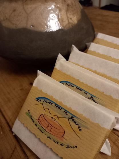 Des savons emballés posent fièrement devant un pot en raku.
