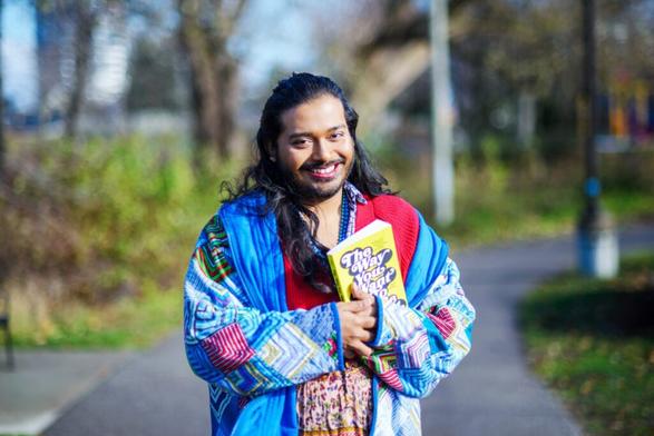 Photo of Aashay Dalvi smiling and posing with a book in Cherry Park.