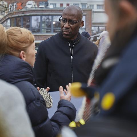 Berliner Kultursenator Joe Chialo mit gerunzelter Stirn im Gespräch mit einer demonstrierenden Person, die von hinten zu sehen ist und bekräftigend gestikuliert.