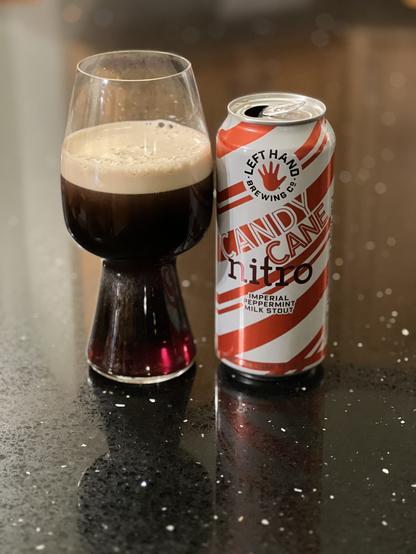A stout glass full of dark beer next to a pint can wrapped in candy cane red and white diagonal stripes. The red LeftHand logo is top center