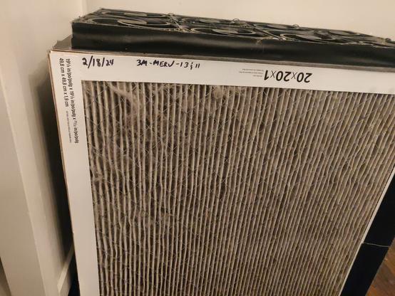CR Box, looking at a 20x20x1 3M MERV-13 filter. There are black PC fans on top. The date it was constructed and put into use ("2/18/24", so it is roughly 10 months old) is written on it.

The filter material (folded into pleats) are a dark grey, almost black. There's also wads of cat hair all over the pleats.