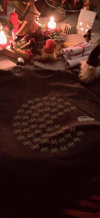 Auf einem adventlich geschmückten Tisch liegt ein graues T-Shirt mit folgendem Aufdruck:

Viele Fahrräder in Form eines Packman verfolgen ein Auto