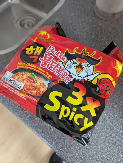 A packet of Buldak 3x spicyu noodles on top of a grey kitchen counter