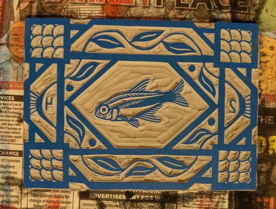 An inked block showing a fish surrounded by a geometric pattern of leaves and scales. The ink is blue