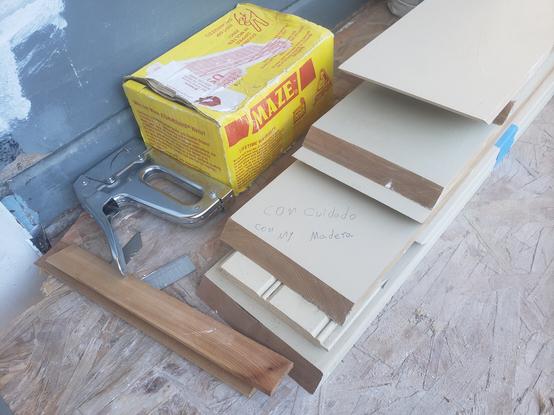 Elementos de carpintería (maderas, grapador, una caja) en un sitio de construcción con el citado mensaje escrito sobre la madera.