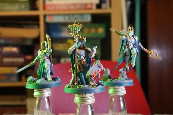 Three models from the game warhammer underworlds. They're clad in white with blue cloaks. The have different weapons but look mostly like they're in the middle of doing some magic. Sidelit in green from the left.