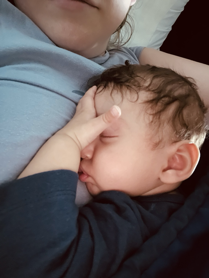 An infant is sleeping with their hand against their forehead. They are resting against their parent's chest.