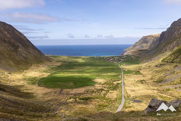 View from a hiking path down into a small valley which ends at the seaside. Little village at the end of the road, colorful houses. Mountains rising left and right.