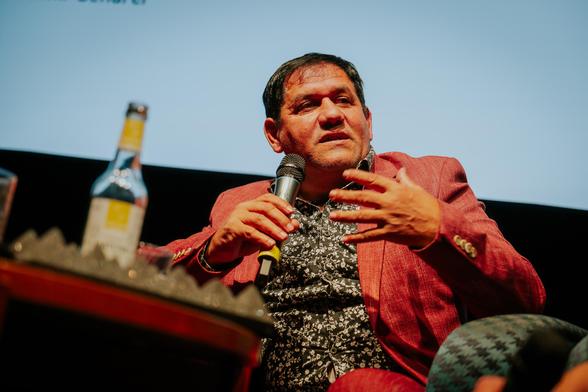 A gentleman in a red jacket is talking to a microphone in a cinema.