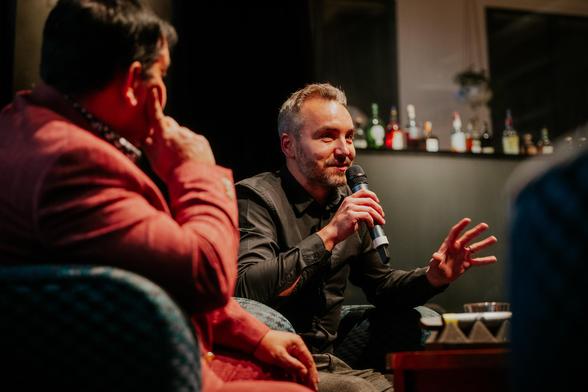 A man in a black shirt talking to a microphone in a cinema,