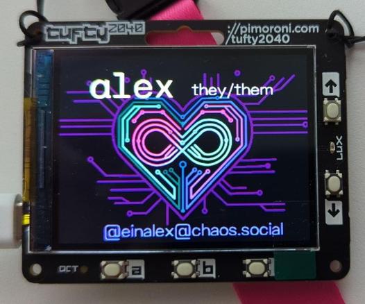 This is a photo of a pimoroni tufty 2400 electronic conference badge. It has some buttons around the parameter. The middle is taken up by a 4:3 screen.
The screen shows in the background the relationship geek logo, a heart embedded in circuit lines, featuring an infinity symbol in the middle.
Around the heart, I added some text: "alex they/them ... @einalex@chaos.social".