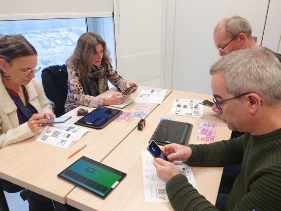 Photo de 4 personnes autour d'une table qui travaillent avec des tablettes, des fascicules et une carte électronique Microbit.