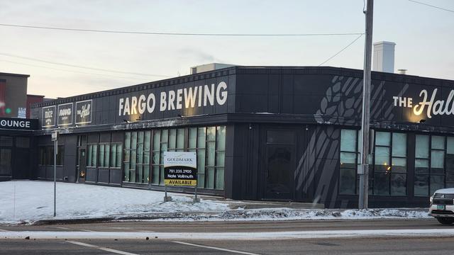 An industrial building with Fargo Brewing painted on the side, and a for sale sign out front.