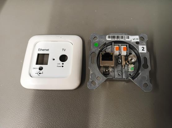 Auf einem grauen Labortisch liegt eine "Digital Devices EOC 2000" Einbaudose. Sie verfügt über einen Ethernet-Anschluss, einen 5,5mm Stromversorgungsanschluss (24V=), einen IEC-Antennenanschluss und innenliegend Federkraftklemmen für Koaxial in und out. Bei out hängt ein Abschlusswiderstand.

Links davon die Abdeckung, von mir angepasst um in Reflex Si Rahmen zu passen ohne Adaptierung.