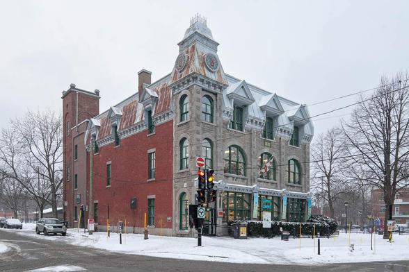 Exterior of a three-storey Beaux-Arts building, with a stone-clad main facade to the right and a simpler, brick facade to the left. A narrow square tower marks the angle, and another brick tower is seen at the back. There is snow on the ground around the building.