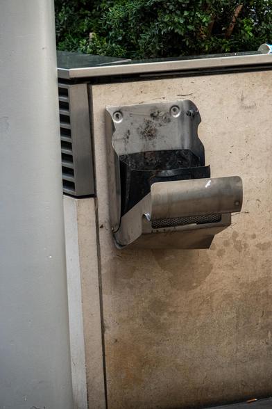A metal wallside ashtray looks like a horrified face with it's mouth wide, due to the way it has fallen open.