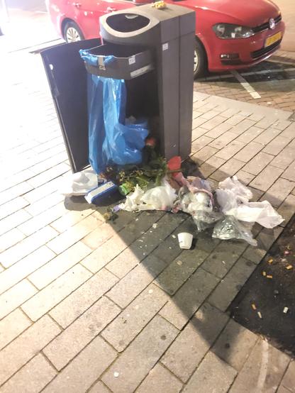 Ein aufgebrochener Mülleimer mit davor verteiltem Müll