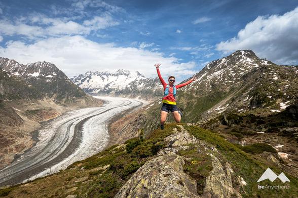 Woman in trailrunning clothes jumping high in front of the huge Aletsch Glacier.