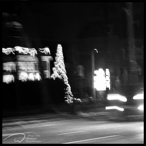Blurry photo of a Christmas tree with lights and the headlights of a moving car at night.