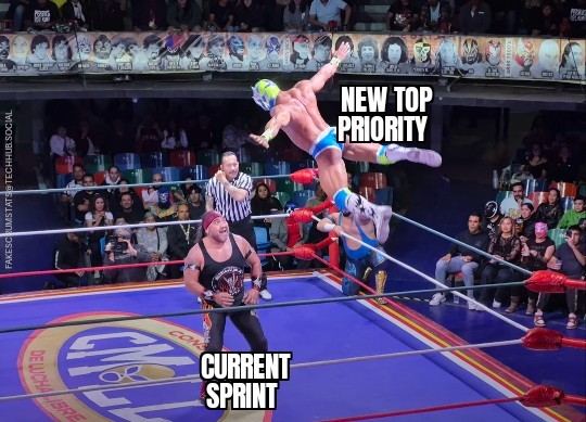 Photo of a wrestling ring. One wrestler (labeled current sprint) standing looking up at his opponent (labeled new top priority) who is flying through the air at him.