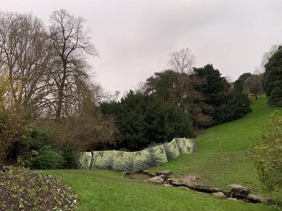 Aux Buttes Chaumont, parc du 19 eme arrondissement de Paris, une palissade imprimée de faux arbres cache des travaux.