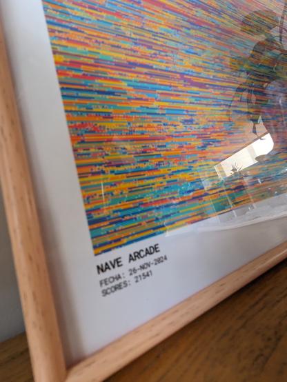 Detail photo of a corner of the framed print. You can see the text "NAVE ARCADE. FECHA: 26-NOV-2024. SCORES: 21541"