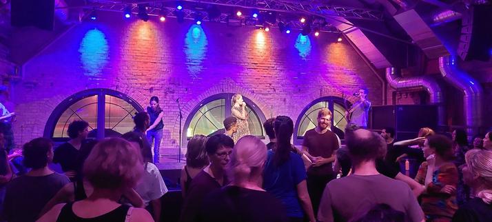 Photo of the stage. You see to musicians and the host. In front of the stage the crowd dancing scottish reell.