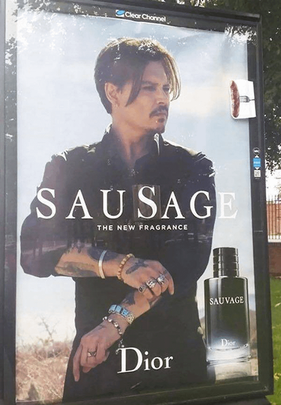 Large poster on a UK bus stop featuring an image of actor Johnny Depp with short hair with a floppy fringe looking to the right while wearing a black shirt and appearing to roll up one of his sleeves. His exposed forearms show tattoos and bead bracelets and he wears many silver rings on his fingers.  In large white capital letters across the centre it says SAUVAGE  but someone has added a large S in similar font to make it say SAUSAGE At top right level with his head is a small picture of a sausage on a fork which has been added. This was a very widespread bit of vandalism for these ads.. I don't think I ever saw one that wasn't turned into SAUSAGE!