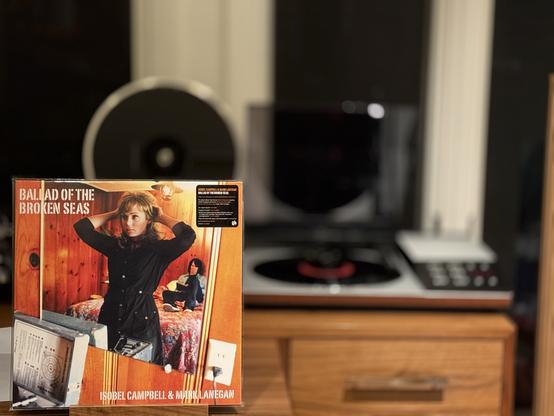 Isobel Campbell & Mark Lanegan - Ballad of the Broken Seas LP cover.

In a cheap hotel room, Isobel looks at herself in the mirror, adjusting her hair in an overcoat, while Lanegan looks on, lying on a bed.

The black LP plays on a vintage, restored Bang & Olufsen Beogram 8002 linear-tracking turntable to the right.