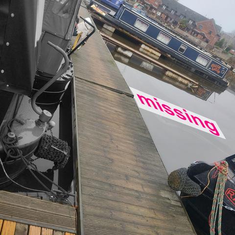 Photo of a dock with moored boats. On one side, there are two boats and a very large gap. There's an annotation on the photo – a white bar with the word "missing" on it – where there used to be a pontoon attached to the main dock by steel frame. It is gone.
