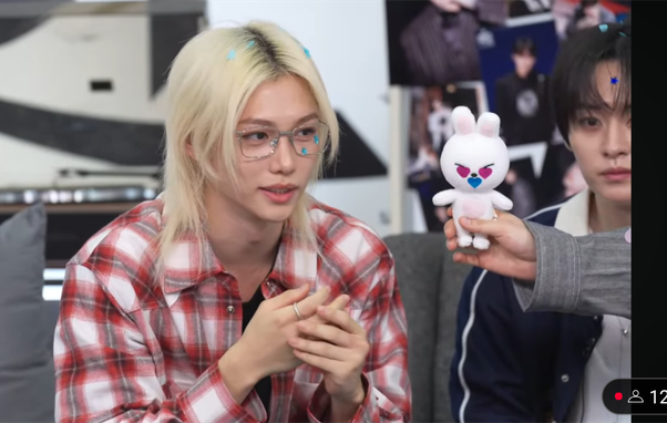 Felix, Lee Know, and Seungmin's hand holding a naked leebit doll with stickers over its eyes and mouth