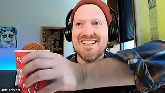Jeff Triplett dunks a stroopwafel in a red cup of coffee while smiling menacingly.