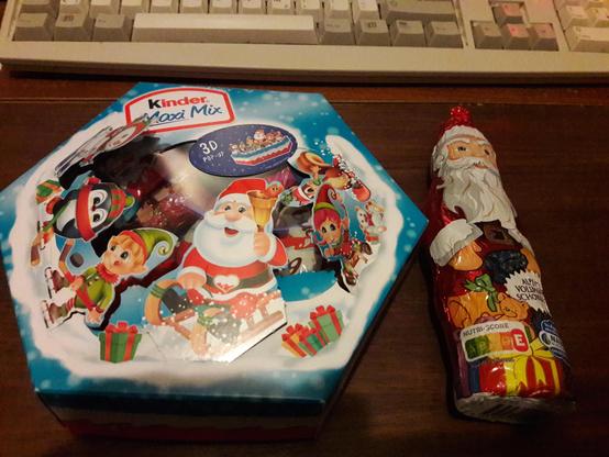 Ein Schokoladennikolaus, der auf einem Wohnzimmertisch liegt. Daneben steht eine Schachtel mit weiteren Süßigkeiten aus Schokolade.