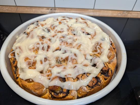 Eine große runde Emailleform gefüllt mit Hefeschnecken, die mit einem Guss aus Frischkäse und Puderzucker bedeckt sind