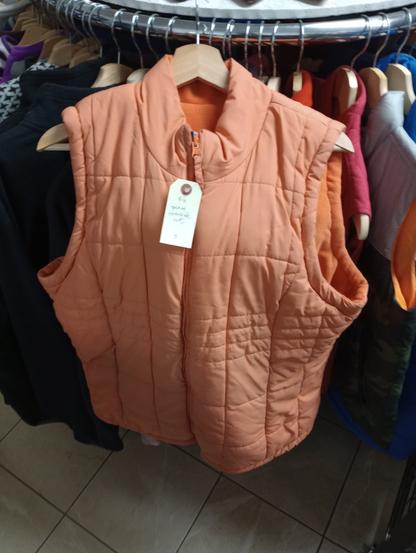 a peach coloured puffy vest hangs on a rack full of winter vests