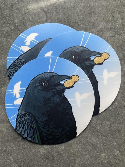 Illustrated Crow sticker – the crow is holding a peanut, silhouettes of other crows and powerlines against a blue background